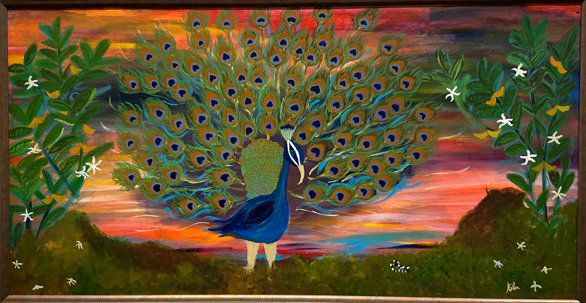 A blue peacock fans its green eyespotted tail on a grassy hill under an orange and pink sunset, between leafy flowering branches, in a wood frame.