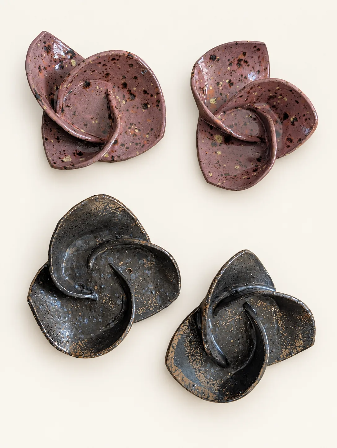 Four glossy ceramic blooms of curling, folded petals: two speckled rose pink ones above and two charcoal ones flecked with bronze below.