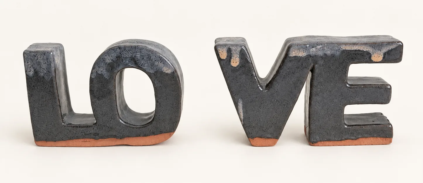 Two charcoal glazed ceramic bookends shaped as chunky block letters, with pale glaze drips along the top and bare terracotta clay showing at the base.