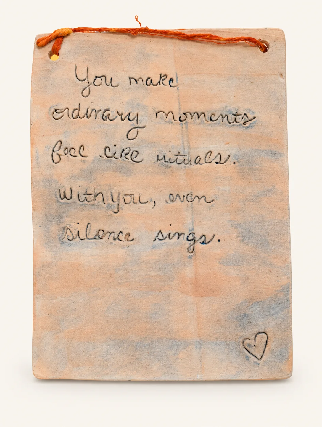 Rectangular peach clay tablet with a soft blue-gray wash, inscribed in cursive handwriting with a small heart, hanging from an orange cord.