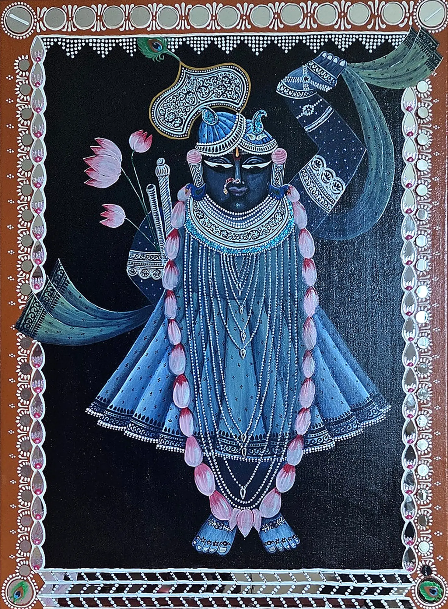A dark blue-faced deity with one arm raised, in a blue robe, pearl strands and a pink lotus garland, inside an orange border set with round mirrors.