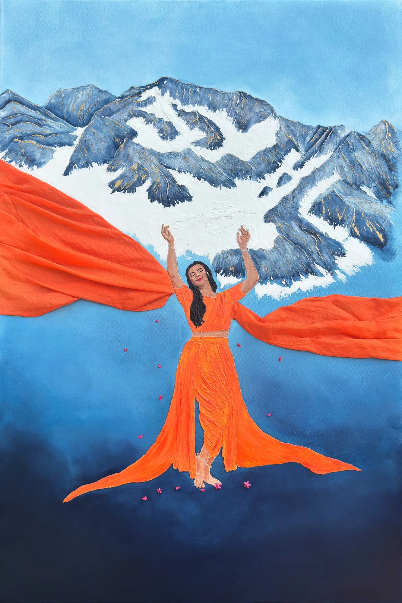 A woman in orange with arms raised and eyes closed, orange fabric streaming to both sides, before a snowy blue-gray mountain, pink petals falling.